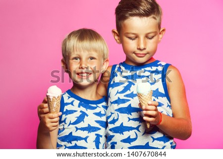 Tasty summer obsession concept. Happy young handsome hipster boys wearing sleeveless shirts with sharks, hugging, eating melting ice cream in waffle cone over pink colour background. Studio shot