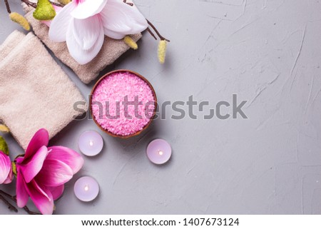 Towels, sea salt in bowl, burning candles and pink magnolia flowers on grey textured background. Spa concept. Selective focus. Place for text. Flat lay.