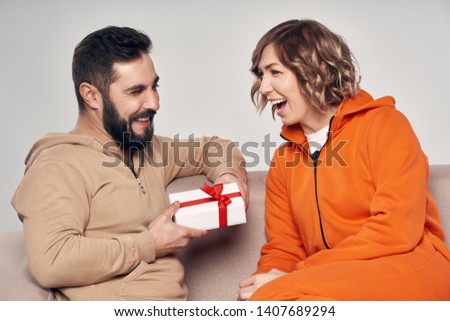 Holiday, celebration and family . Smiling man surprising his girlfriend with present at home sitting on sofa