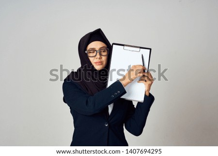 Hijab woman with a folder-tablet showing a pen on a white blank on a gray background free place                              