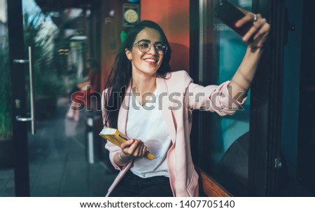 Cheerful woman in optical spectacles for provide eyes protection smiling at camera and clicking selfie pictures for attract followers in social web page enjoying internet connection for networking