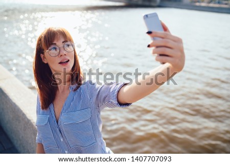 Good looking hipster girl dressed in casual wear clicking selfie photos for creating media content via cellphone camera, attractive woman in optical spectacles posing and making pictures via app