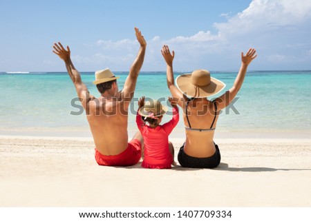 Rear View Of Family Sitting On Sand Raising Their Hands Enjoying On The Beach