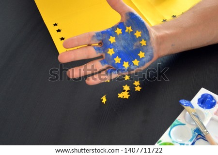 close up on the hand - a person is drawing the european flag on his hand with blue color and yellow paper stars - concept to celebrate europe and the freedom
