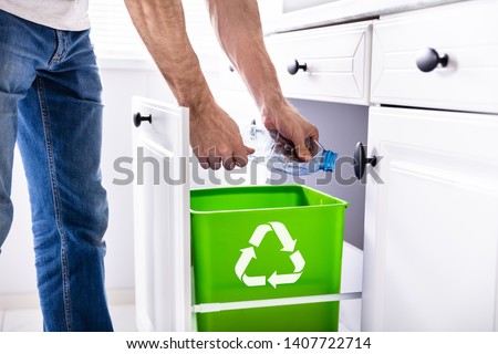 Low Section Of Man Throwing Empty Plastic Bottle In Recycling Bin In The Kitchen