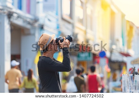 Asian man holding camera and taking   picture of sino portuguese architecture building on famous sunday walking street  in phuket old town.
Tourist sightseeing old town ,traveling concept.