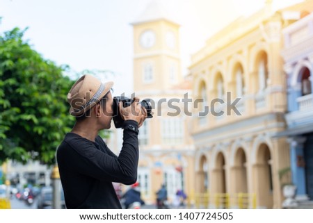 Asian man holding camera and taking   picture of sino portuguese architecture building on famous walking street  in phuket old town.
Tourist sightseeing old town ,traveling concept.
