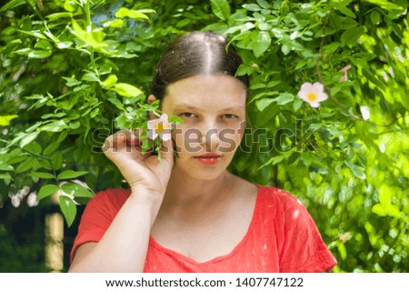 Portrait of happy girl in orange blouse against the backdrop of flowering wild rose bush in sunlight. Lens natural light effect. Selective focus, shallow depth of field. Art image of nature, bokeh