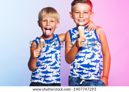 Tasty summer obsession concept. Happy young handsome hipster boys wearing sleeveless shirts with sharks, hugging, eating melting ice cream in waffle cone over pink & blue background. Studio shot