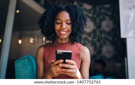 Happy female teenager in casual wear sending sms message via smartphone device using 4g wireless connection for chatting, positive woman searching new application for editing photos on cellular