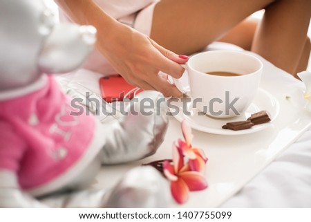 Close up photo of a  woman hand with Coffee cup and a plate with a pieces of milk chocolate on the bed. Happy morning concept