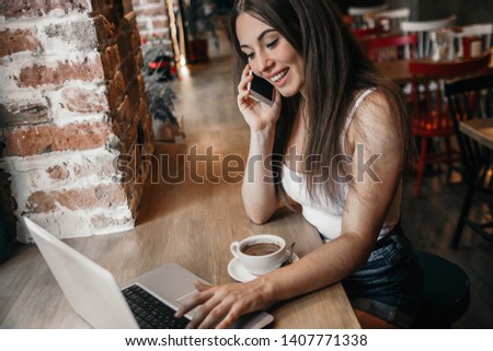 Business woman using phone, working on a laptop and drinking coffee in a cafe.
