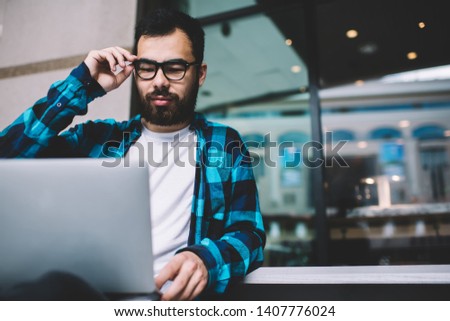 Concentrated male graphic designer using application for job on laptop computer working on freelance, man in eyewear studying online downloading files from networks on netbook via modern netbook