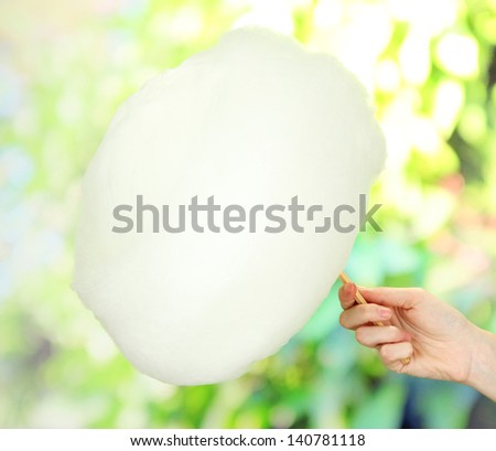 Hand holding stick with cotton candy, on bright background