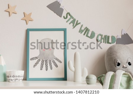 Cozy scandinavian nursery interior with mock up photo frame, plush octopus, cacti and children's  accessories. Hanging stylish inscription and stars on the white background wall. Template. Real photo.