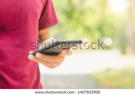 close up handsome man use left hand typing mobile phones and touch screen working with app devices in park with sunrise and green blur nature background.