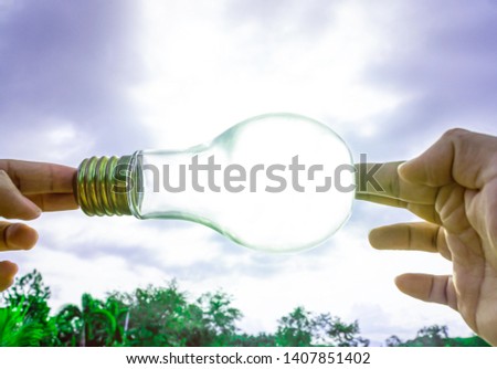 Use hand hold the electric light bulb for electricity for life concept in vintage tone. Retro Incandescent lamp with green nature against the blue sky.