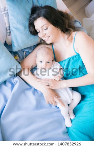 Young mother and little cute baby lying on a bed with a blue blanket at home
