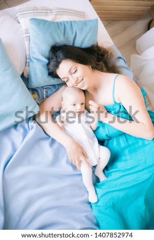Young mother and little cute baby lying on a bed with a blue blanket at home
