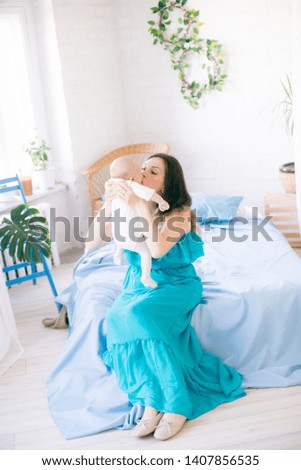 
Young mother and little cute baby at home on bed with blue bedspread and pillows
