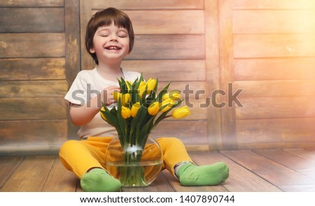 A small child with a bouquet of yellow tulips. A boy with a gift of flowers in a vase. A gift for girls on female holiday with yellow tulips on the floor.
