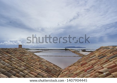 Evening landscape picture of ponds or saltpans in traditional salt production in Trapani in island Sicily during the sunset with cloudy sky and calm sea. Riserva naturale integrale Saline di Trapani. 