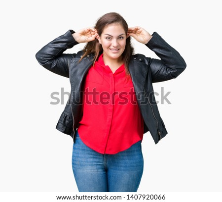 Beautiful plus size young woman wearing a fashion leather jacket over isolated background Smiling pulling ears with fingers, funny gesture. Audition problem