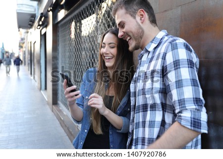 Funny couple checking smart phone online content standing in the street