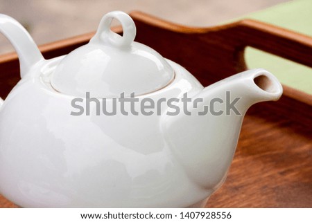 An elegant simple plain white english teapot on an organic wooden tray, closeup / macro. Serving tea in a traditional simplistic manner, tea drinking concept.