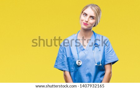 Young beautiful blonde doctor surgeon nurse woman over isolated background making fish face with lips, crazy and comical gesture. Funny expression.