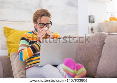 beautiful woman sitting at home on the sofa - tired woman with fever feeling upset with a napking in her hand - woman feeling cold at winter - with her pc or laptop on hers legs