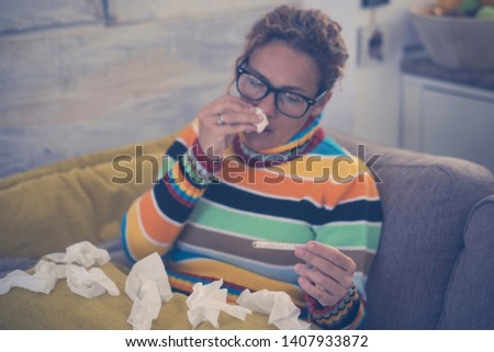 woman feeling cold, freezing, with napkin in a hand, wrapped in blanket, sitting on the sofa. Unhappy upset tired woman is sitting on a sofa at home suffering from a cold and using napkins