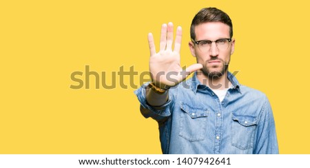 Handsome man wearing glasses doing stop sing with palm of the hand. Warning expression with negative and serious gesture on the face.