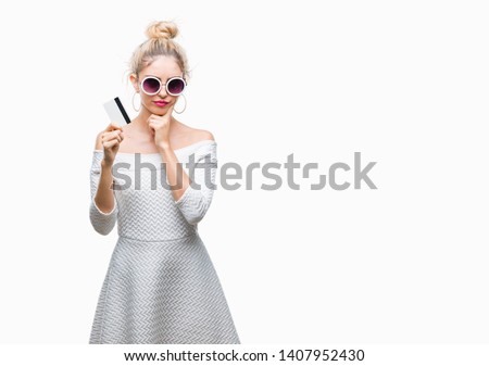 Young beautiful blonde woman holding credit card over isolated background serious face thinking about question, very confused idea