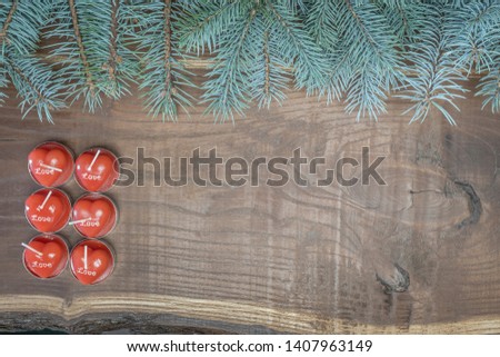 Red candles in the shape of a heart and fir branches on a woody background