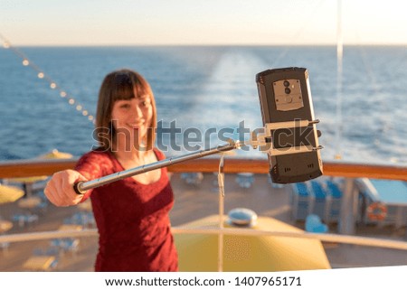 A young girl, with piercings and a garnet blouse takes selfies on board a cruise ship.