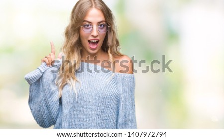 Beautiful young blonde woman wearing sunglasses over isolated background pointing finger up with successful idea. Exited and happy. Number one.
