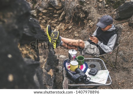 View from above young boy with hat, sitting with legs raised resting wall. Young male looking smartphone chatting with friends anywhere Explorer in search adventure Outdoor life healthy hobby concept