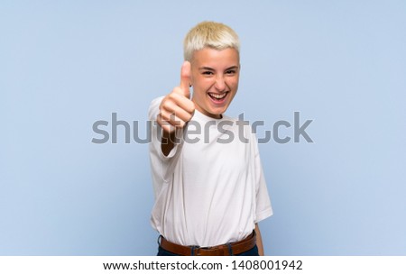 Teenager girl with white short hair over blue wall with thumbs up because something good has happened