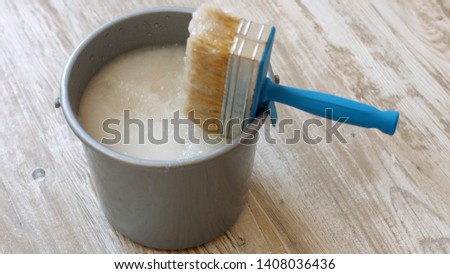Wallpaper paste brush and grey bucket. Bucket with wallpaper glue and brush on new wooden floor. Apartment renovation concept. Royalty-Free Stock Photo #1408036436