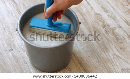 Male hand holding brush for applying wallpaper paste. Wallpaper paste in bucket. How to hang a wallpaper. Royalty-Free Stock Photo #1408036442
