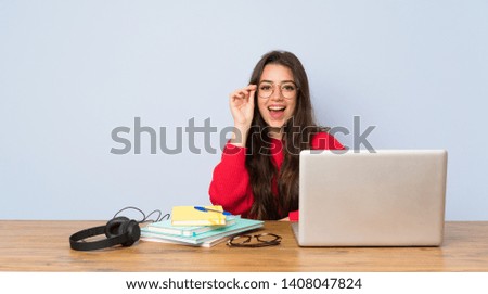 Teenager student girl studying in a table with glasses and surprised