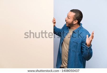 Colombian man holding an empty placard with surprise facial expression