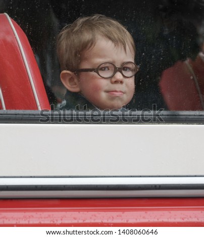 A little boy with round glasses looks through the bus window. Small boy leaving from grandma (vintage processing, noises, film photo)