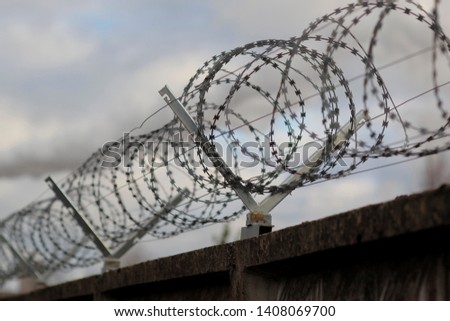 Barbed wire and concrete wall on gray sky background