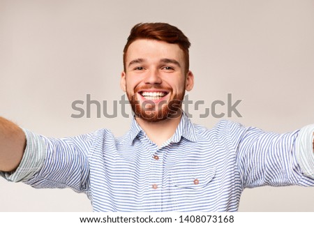 Selfie everywhere! Handsome young caucasian man photographing himself on camera and widely smiling, standing against beige background Royalty-Free Stock Photo #1408073168
