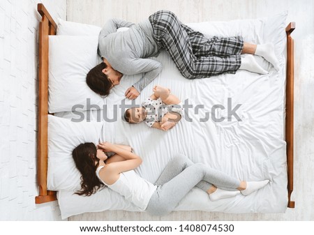 Funny family with one newborn child in the middle of bed, parents sleeping on sides, top view Royalty-Free Stock Photo #1408074530