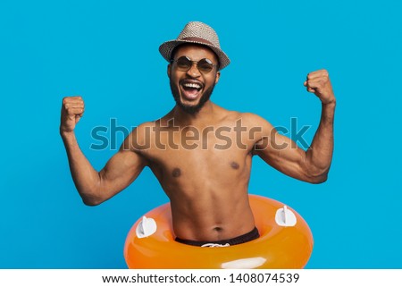 Emotional african american man wearing inflatable ring, enjoying summer vacation, blue background