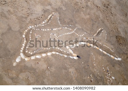 Sand sculpture dolphin decorated with shells on the beach. Seashore background. 