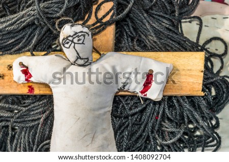 black magic doll hanging on a christian cross and needles dipped into it's body